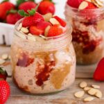 Glass jar filled with almond strawberry overnight oats topped with fresh strawberries and sliced almonds on a rustic table