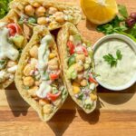 Chickpea and veggie-filled Greek pita pockets with tzatziki sauce on a wooden board