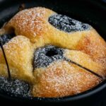Close-up of a low-carb cherry almond pancake pot in a black ramekin, topped with powdered sugar and baked cherries