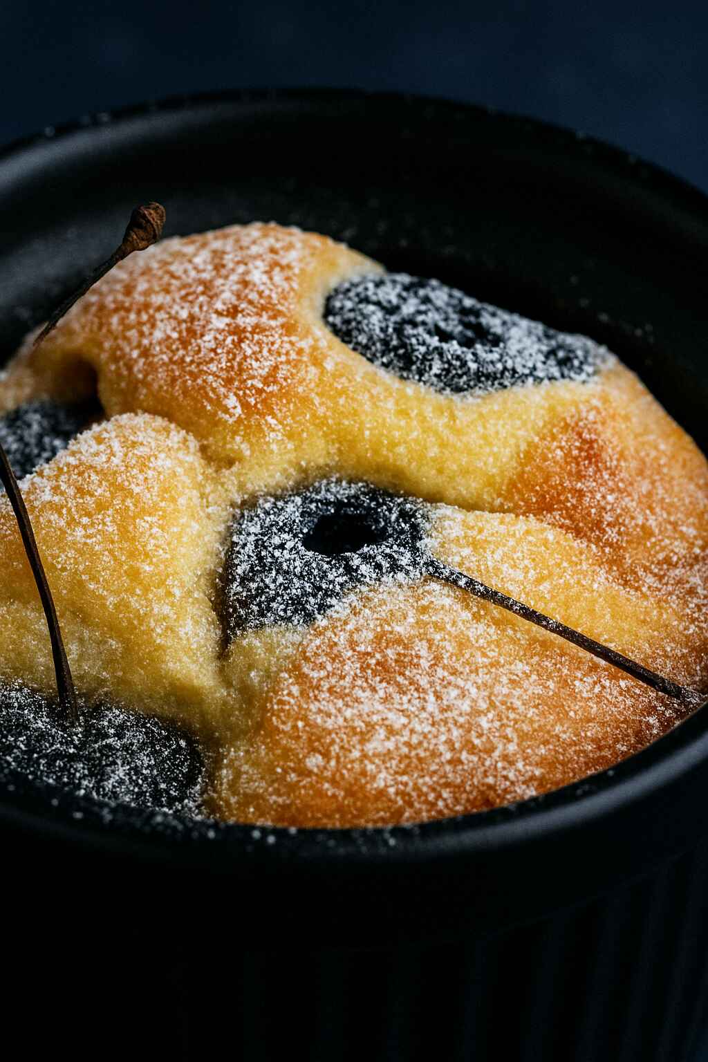 Close-up of a low-carb cherry almond pancake pot in a black ramekin, topped with powdered sugar and baked cherries