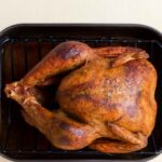 Whole roasted rotisserie chicken in a black roasting pan, ready for meal prep