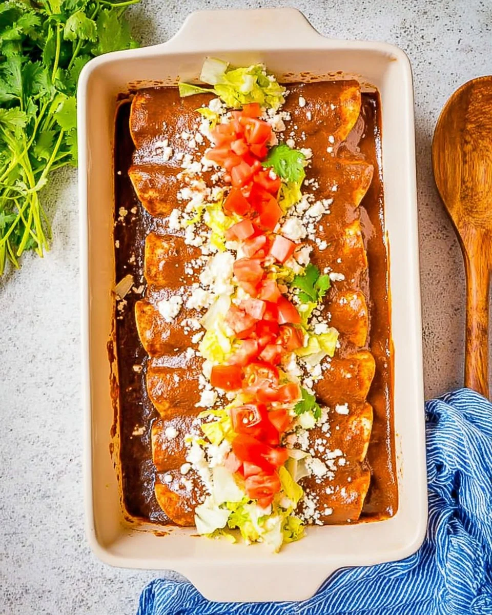 Plate of Chicken Mole Enchiladas topped with sauce and garnished with fresh herbs.